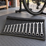12-piece ratcheting combination spanner set in a canvas tool roll beside a bicycle in a garage